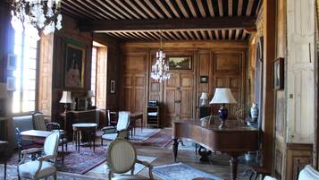 Une pièce spacieuse avec des boiseries, un lustre et divers sièges, notamment un canapé, des fauteuils et une table.