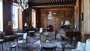 A spacious room with wooden paneling, a grand piano, multiple chairs, and a chandelier.