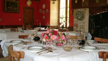 A dining room with tables set for a meal, featuring white tablecloths, silverware, and floral centerpieces.