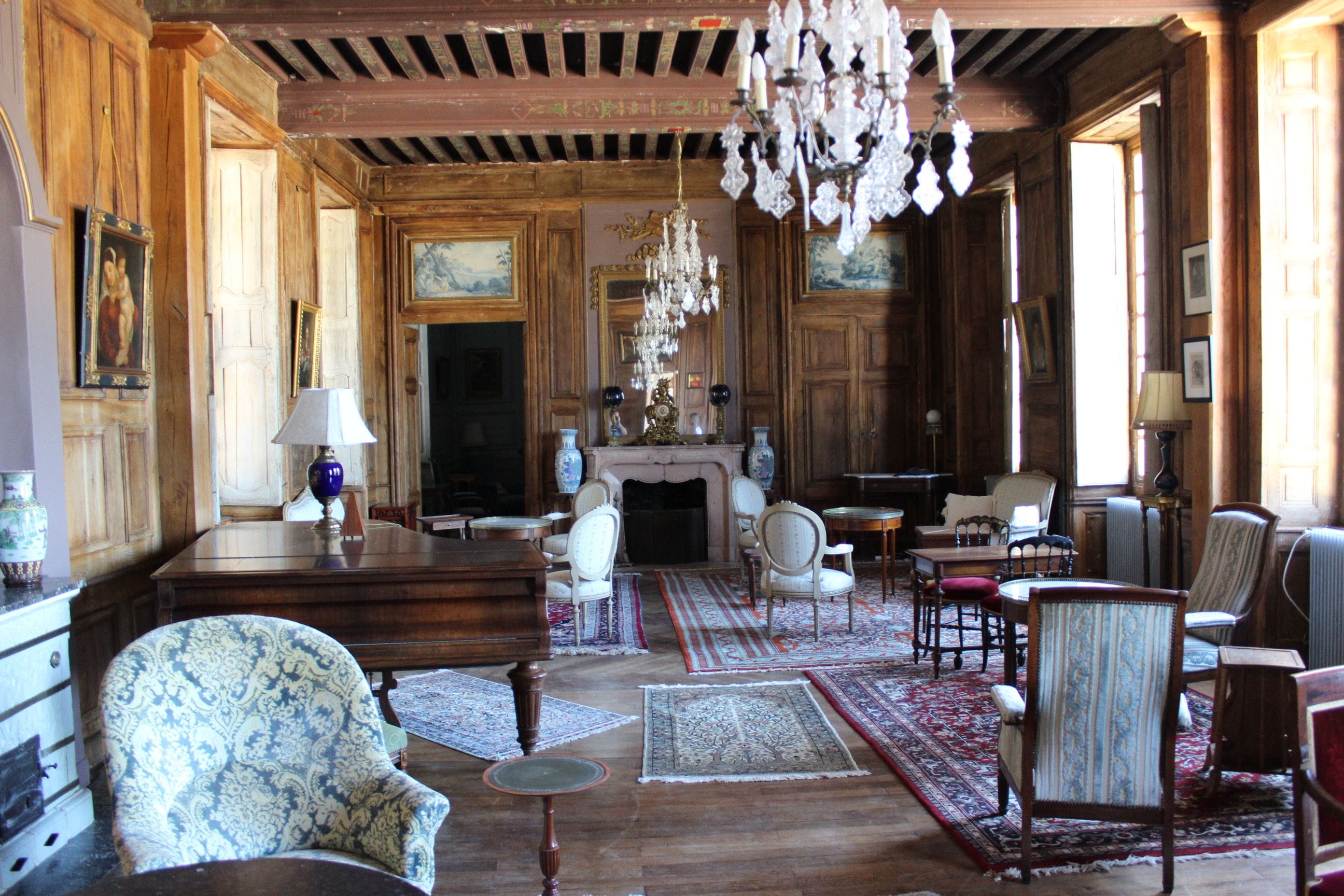 Une pièce spacieuse avec des boiseries, une cheminée, plusieurs coins salon et un lustre.