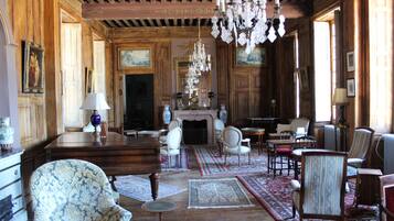 Une pièce spacieuse avec des boiseries, une cheminée, plusieurs coins salon et un lustre.