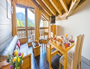 Una habitación acogedora con techo de madera, un sofá, una mesa de comedor con alimentos para el desayuno y un televisor sobre un mueble.