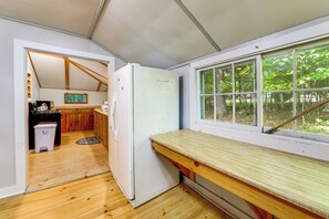 Une cuisine de taille réduite, dotée de meubles en bois, d’un réfrigérateur blanc et d’une fenêtre donnant sur une forêt.