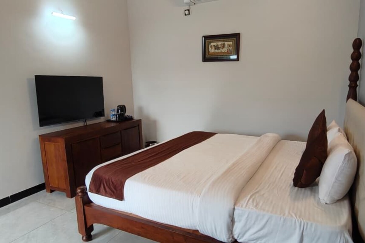 A bedroom with a bed, a television on a stand, a dresser, and a framed picture on the wall.
