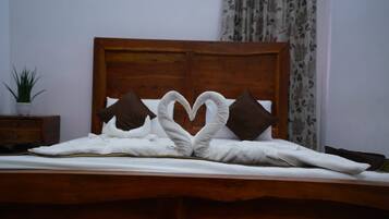 A bed with a wooden headboard, two pillows, and a towel arranged in a heart shape.