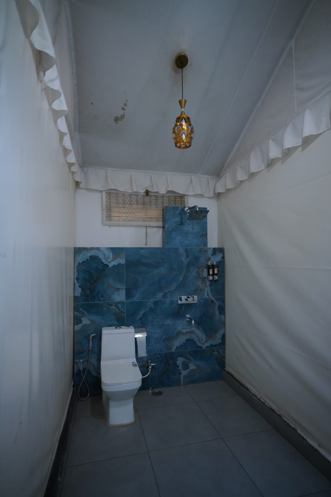A bathroom with a white toilet, a blue marble wall, and a hanging light fixture.