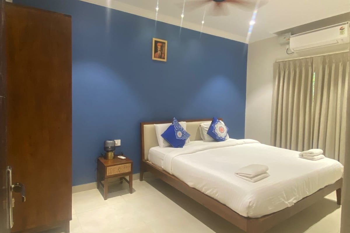 A hotel room with a bed, a bedside table, a ceiling fan, and a window with curtains.