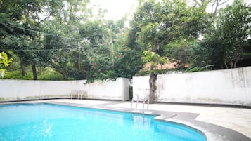 A swimming pool with a white wall and a tree in the background.