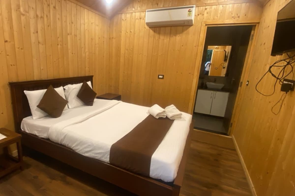 A wooden-paneled room with a bed, a nightstand, a mirror, and a small bathroom.