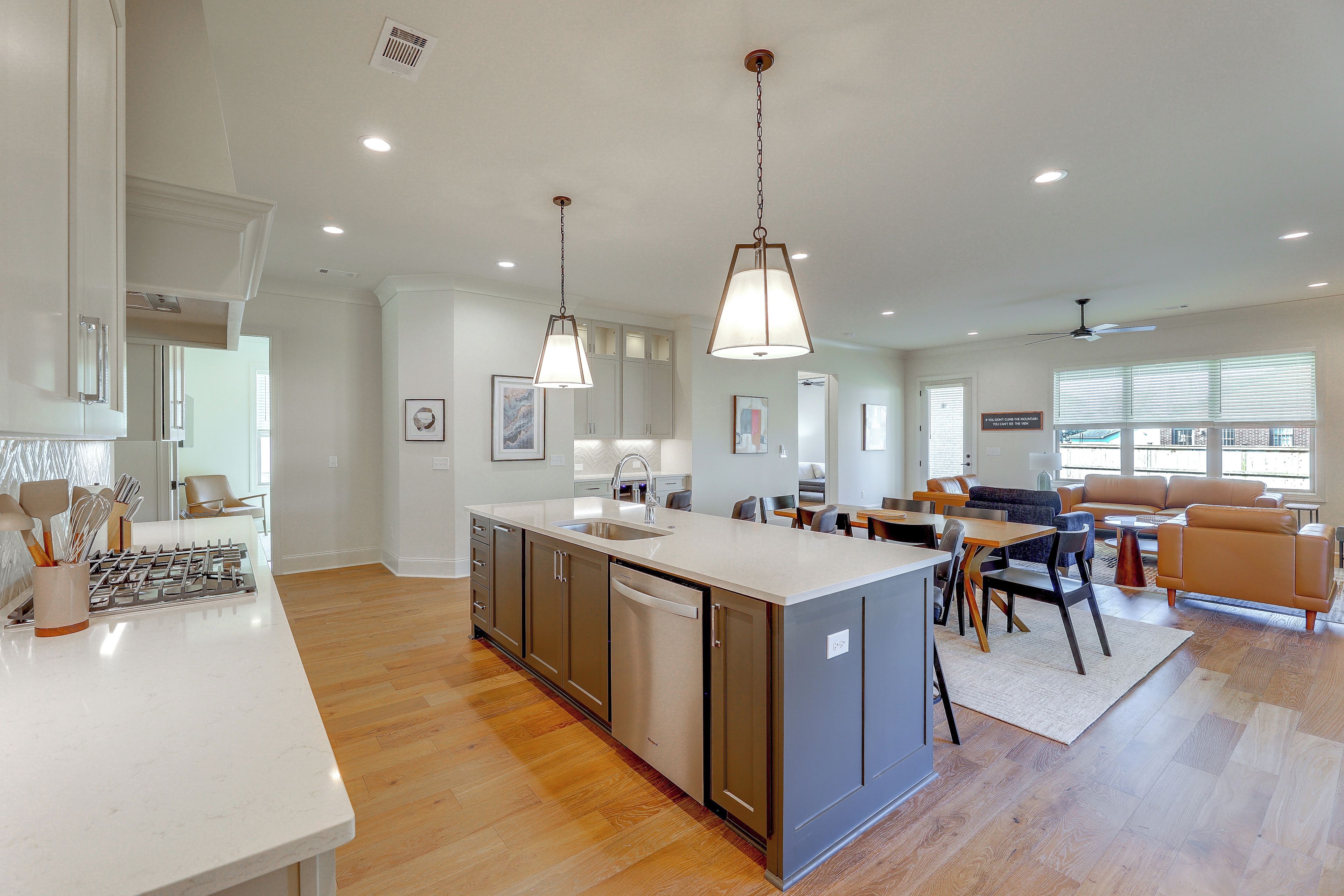 A modern kitchen with a central island, a dining area with a sofa and chairs, and a living room with a large window.