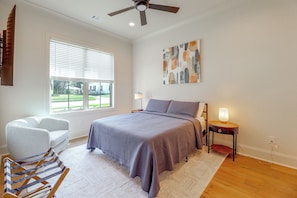 A bedroom with a bed, a chair, a bedside table with a lamp, a ceiling fan, and a window with blinds.