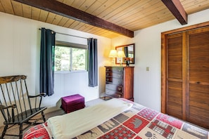 Ein Zimmer mit einem Bett, einem Schminktisch, einem Stuhl, einem Fenster mit Vorhängen und einer Holztür.