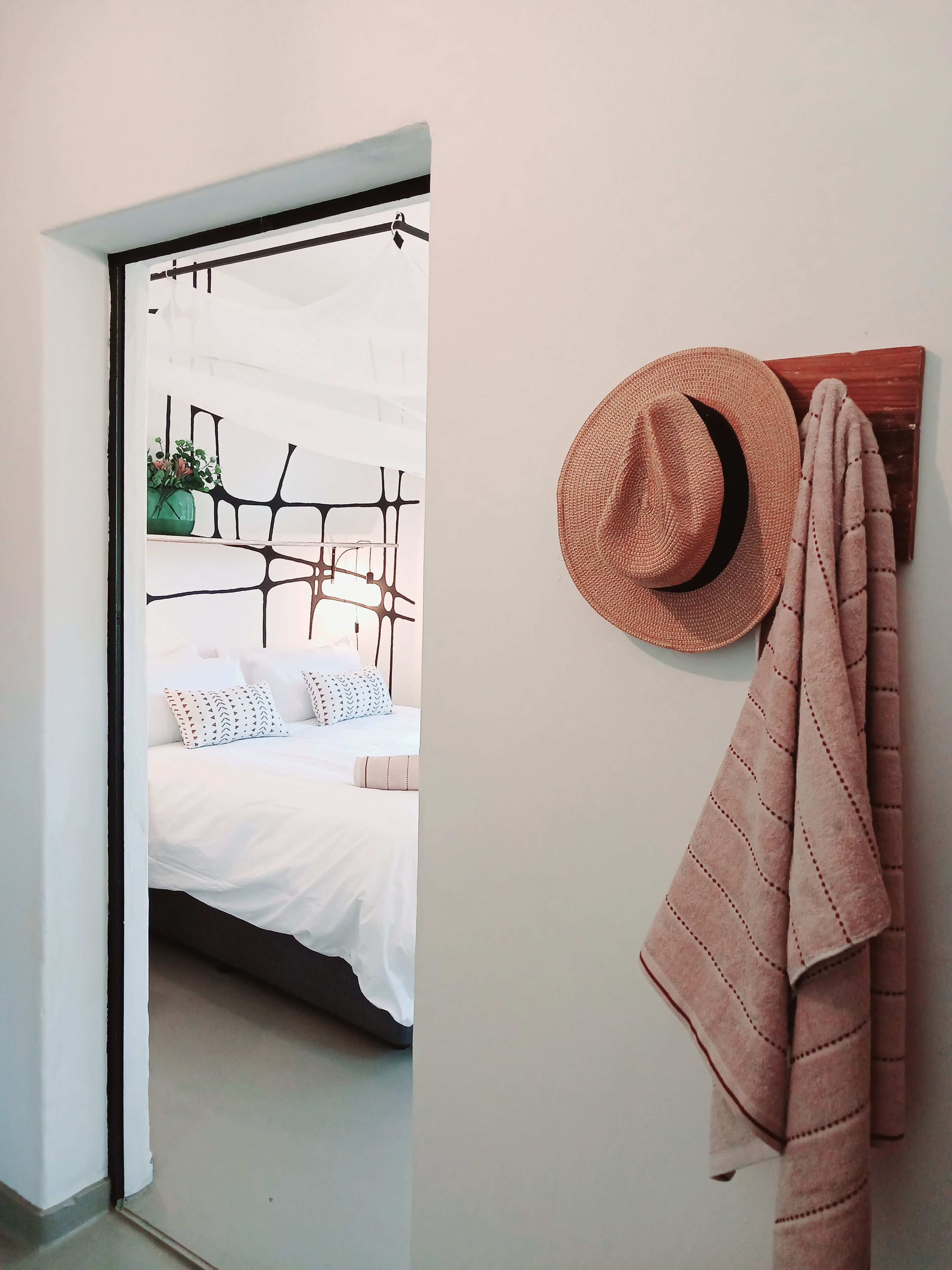 A bedroom with a bed, a hanging plant, and a hat on the wall.