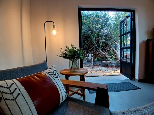 A modern interior with a sofa, a table with a vase of flowers, and a view of a garden through an open door. - A beautiful home in central Livingstone with a Pool near Victoria Falls (Livingstone)
