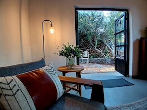 Un interior moderno con un sofá, una mesa con un florero y vistas a un jardín a través de una puerta abierta.