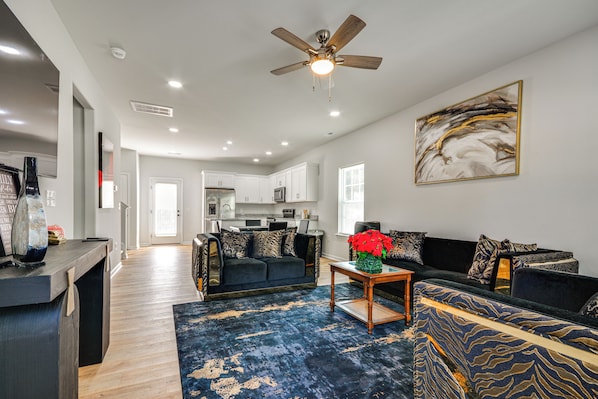 A modern living room with a dark blue patterned rug, a ceiling fan, and a large abstract painting on the wall.