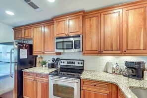 A kitchen with wooden cabinets, a stainless steel refrigerator, a microwave, an oven, and a Keurig coffee maker.