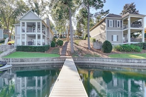 A residential area with a dock leading to a calm water body, surrounded by well-maintained lawns and mature trees.