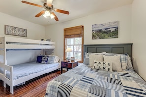 A bedroom with a bunk bed, a single bed, a ceiling fan, a window with blinds, and a landscape painting.