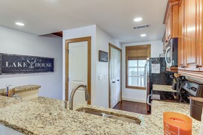 A kitchen with granite countertops, a stainless steel sink, wooden cabinets, and a sign on the wall.
