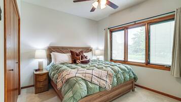 Une chambre à coucher avec un lit, une table de chevet, une lampe, une fenêtre et un ventilateur de plafond.