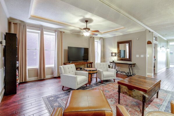 A spacious living room with a flat-screen TV, comfortable seating, a wooden coffee table, and a ceiling fan.