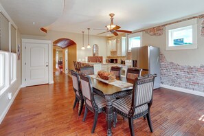 A dining area with a wooden table and chairs, a ceiling fan, and a kitchen in the background.
