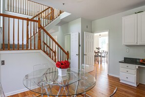 A modern kitchen with a glass dining table, wooden staircase, and white cabinetry. - Spacious Bowie Home Near D.C. Attractions (Bowie)