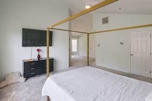 Une chambre à coucher avec un lit à baldaquin, un téléviseur fixé au mur et une commode ornée d’un vase de fleurs.
