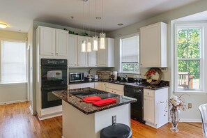 A modern kitchen with white cabinetry, a central island with a red towel, stainless steel appliances, and a view of greenery through the window. - Spacious Bowie Home Near D.C. Attractions (Bowie)