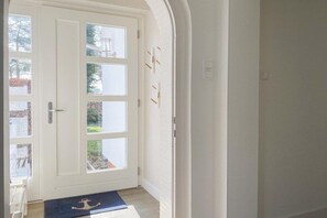 A white door with multiple glass panes, a blue mat with an anchor symbol, and a brick wall with a light switch. - Holiday home with 4 bedrooms (Timmendorfer Strand)