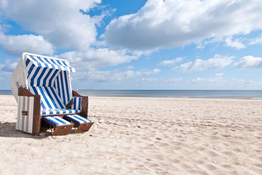 Une chaise de plage avec un coussin à rayures, posée sur une plage de sable fin, sous un ciel dégagé.