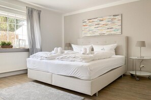 A bedroom with a large bed, a window with curtains, a bedside table with a lamp, and a wall-mounted artwork. - Holiday home with 4 bedrooms (Timmendorfer Strand)