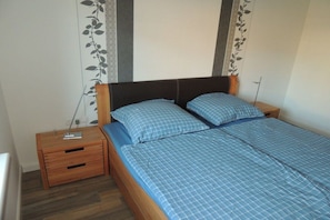 Une chambre à coucher avec un lit en bois, deux oreillers, une table de chevet et un mur orné de motifs de feuilles.