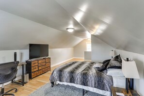 A bedroom with a sloped ceiling, a bed with a patterned bedspread, a desk with a computer, and a television on a dresser. - Nurse-Ready Rental 1 Mi to Franciscan University! (Steubenville)