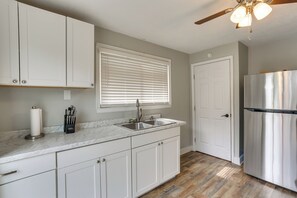 A kitchen with white cabinets, a stainless steel sink, a refrigerator, and a ceiling fan.