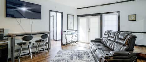 Una sala de estar moderna con un televisor de pantalla plana, un sofá de cuero, un comedor con sillas y un ventilador de techo.