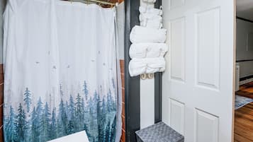 A bathroom with a shower curtain featuring a forest print, a towel rack with folded towels, and a wooden floor.