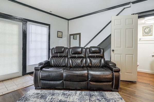 A black leather sofa in a room with a patterned rug, a door, and a window with blinds. - 6 Mi to NCSU! Quiet & Wooded Retreat (Raleigh)