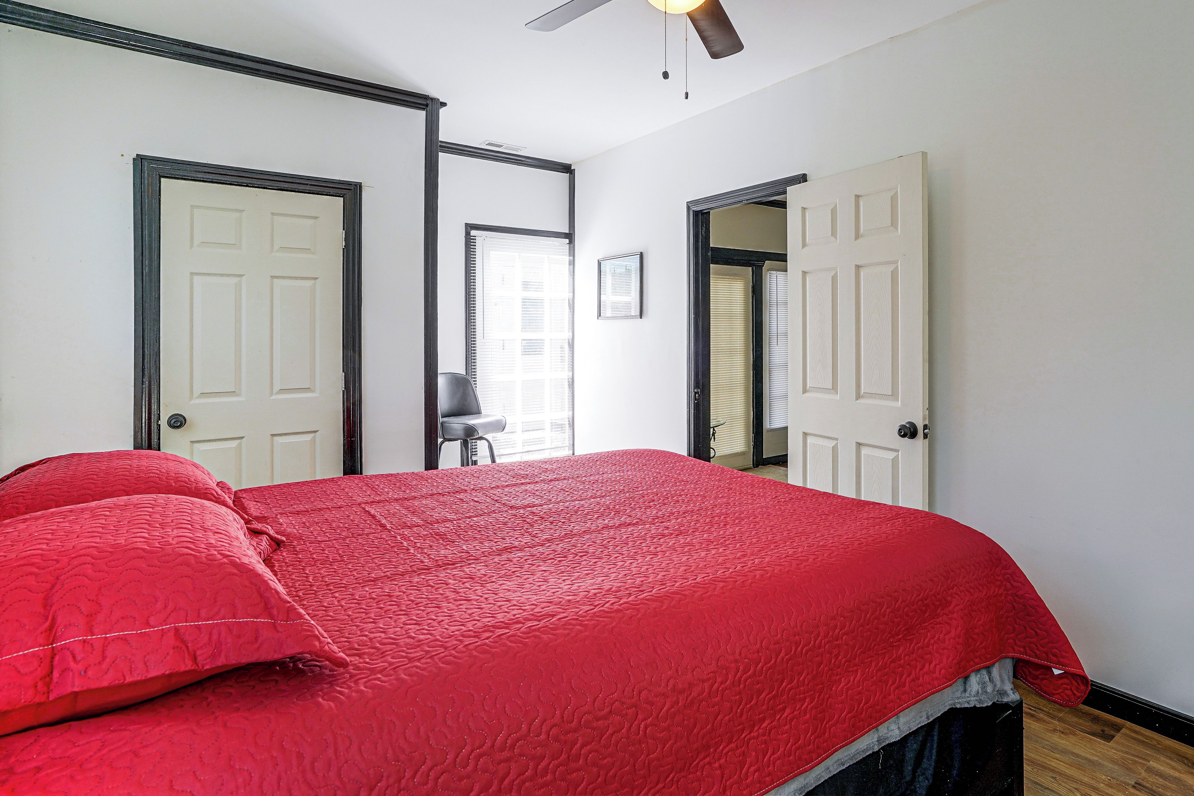 A bedroom with a large bed, two doors, a ceiling fan, and a window with blinds.