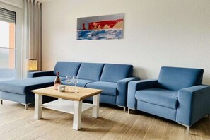 Ein modernes Wohnzimmer mit einem blauen Sofagarnitur, einem Holztisch und einem Bild an der Wand.