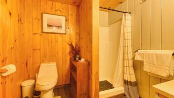 A wooden bathroom with a toilet, a shower, and a sink.
