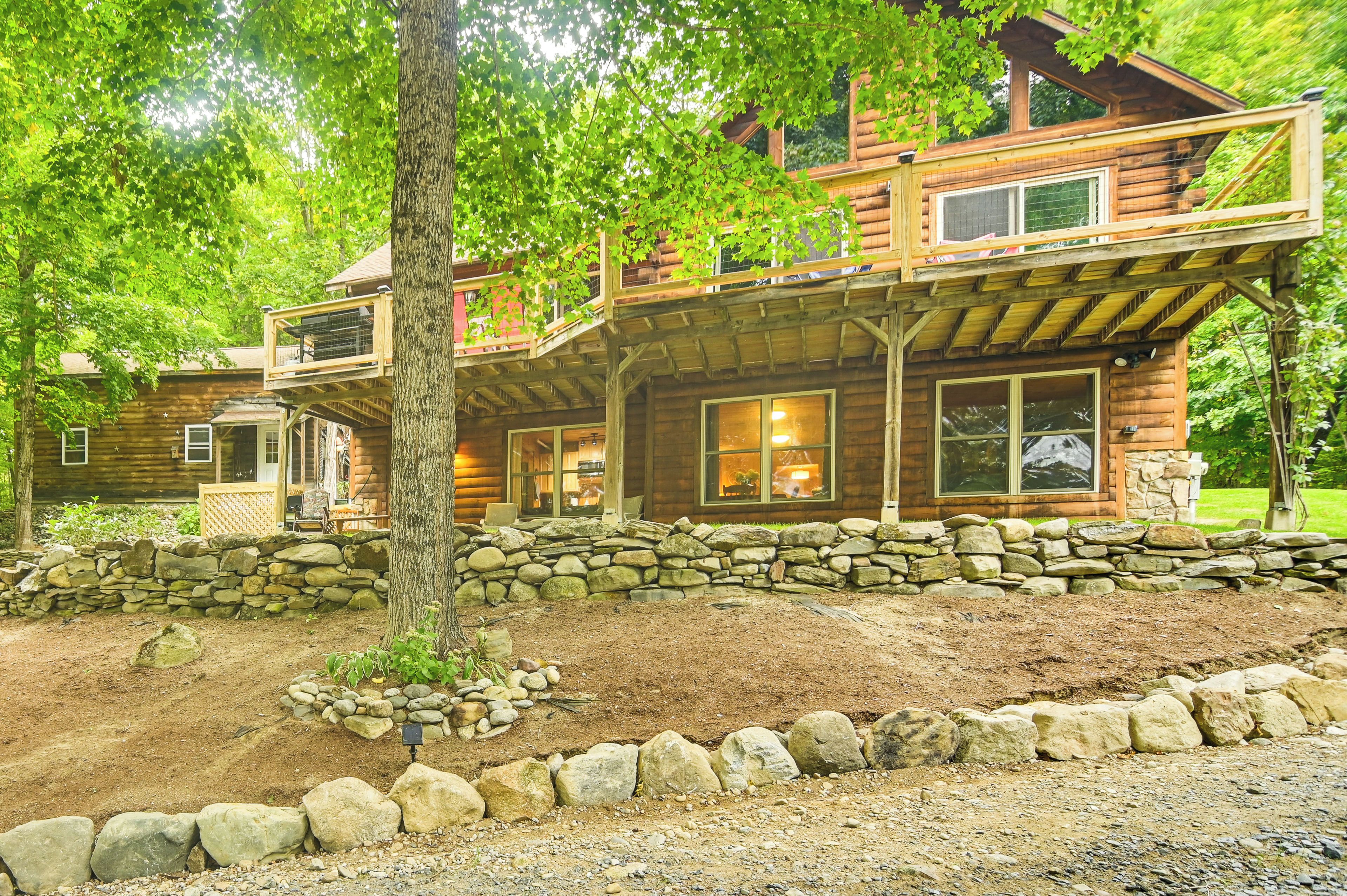 A log cabin with a stone foundation, a wooden deck, and a stone wall surrounding the property.