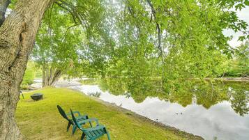 A tranquil lakeside setting with a bench and a picnic table under a large tree.