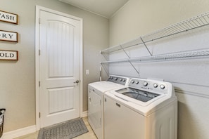 A laundry room with a white door, a washer and dryer, and metal shelves above. - Stylish Home Near Beaches & Golf in Rotonda West! (Rotonda West)