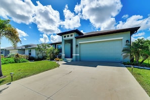 A residential house with a garage, a well-maintained lawn, and a clear sky. - Stylish Home Near Beaches & Golf in Rotonda West! (Rotonda West)