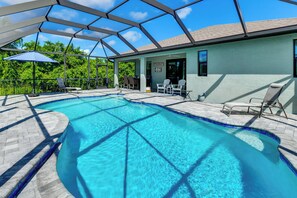 A swimming pool with a covered patio area, lounge chairs, and a view of the surrounding greenery. - Stylish Home Near Beaches & Golf in Rotonda West! (Rotonda West)