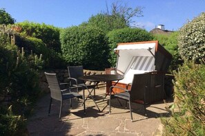 Un espace extérieur aménagé avec une table et des chaises, entouré de verdure et doté d’un patio en pierre.