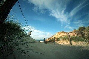 A sandy path with wooden posts, leading towards a dune-covered landscape under a clear sky. - Sonnenkuhle - Ameland 09 (Wenningstedt - Braderup)
