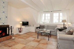 Un salon avec une cheminée, des meubles à rayures, un téléviseur et une fenêtre avec des rideaux.